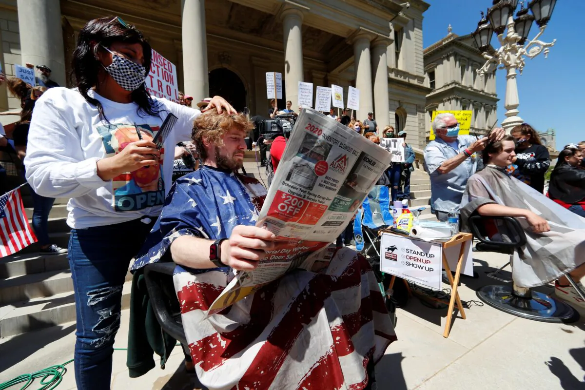 Jody Hebberd, left, gives a free haircut to Reid Scott, as he reads the paper on the steps of the State Capitol as Karl Manke, right, cuts the hair of Parker Shonts during a rally in Lansing, Mich., on May 20, 2020. (Paul Sancya/AP Photo)