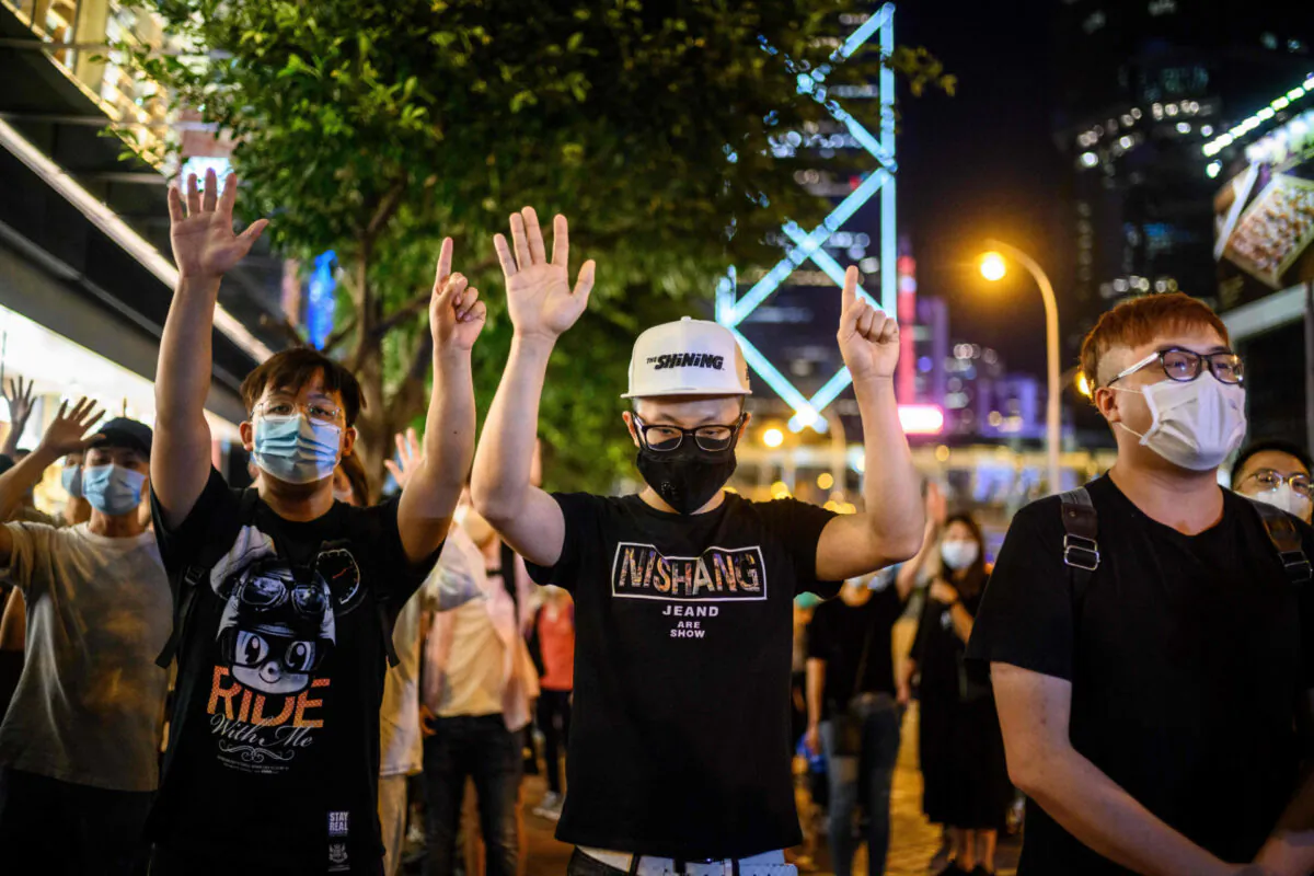 Pro-democracy protesters gesture the slogan 'five demands and not one less' during a vigil outside the Pacific Place shopping mall in the Admiralty area of Hong Kong on May 15, 2020, to mark the 11 month anniversary since a man fell to his death from a scaffolding, during a protest against the Hong Kong government's extradition bill last year. (Anthony Wallance/AFP via Getty Images)