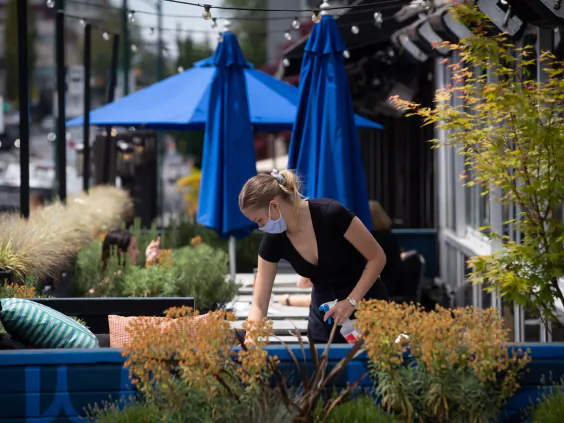 A server wears a face mask while cleaning a table on the patio at an Earls restaurant, in Vancouver, on May 19, 2020. (Darryl Dyck / The Canadian Press)