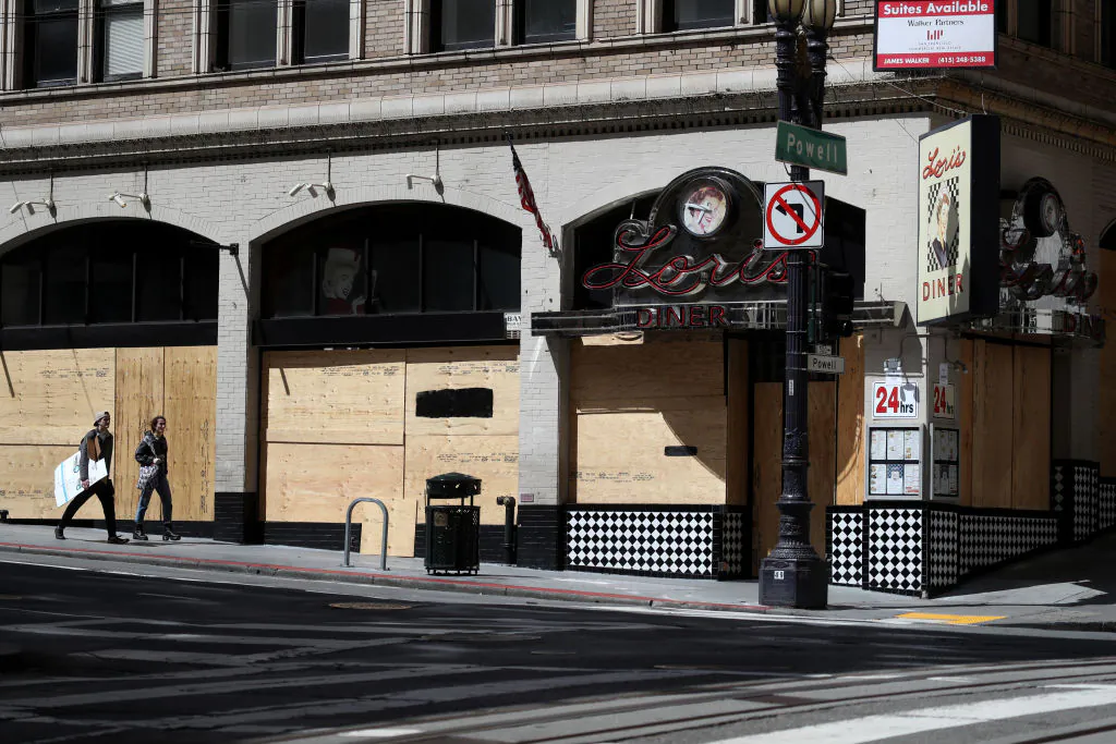 Pedestrians walk by a boarded-up restaurant in San Francisco on March 31, 2020. (Photo by Justin Sullivan/Getty Images)