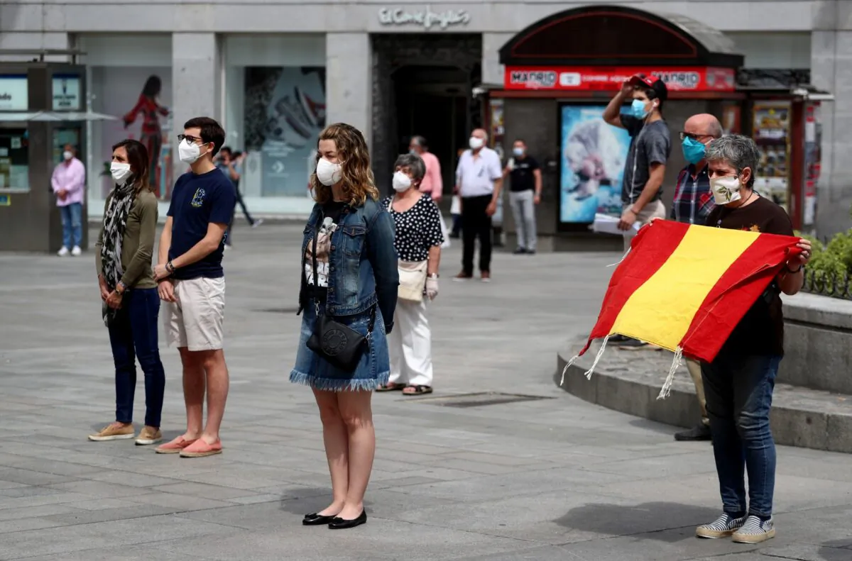 People wearing protective face masks stand during a daily minute of silence to commemorate victims of the CCP Virus, at Puerta del Sol square in Madrid, Spain, on May 26, 2020. (Sergio Perez/Reuters)