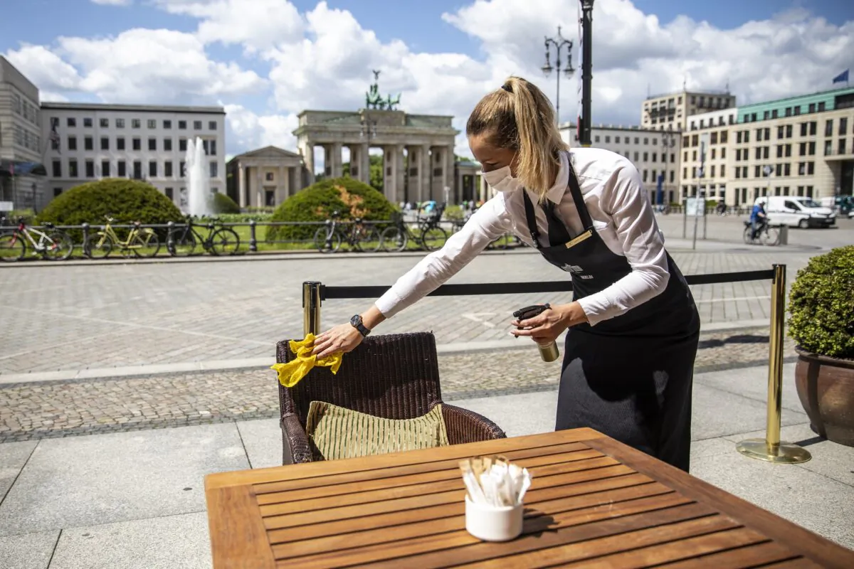 A waitress disinfects a table in a restaurant at the Hotel Adlon Kempinski next to the Brandenburg Gate in Berlin on May 26, 2020. (Maja Hitij/Getty Images)