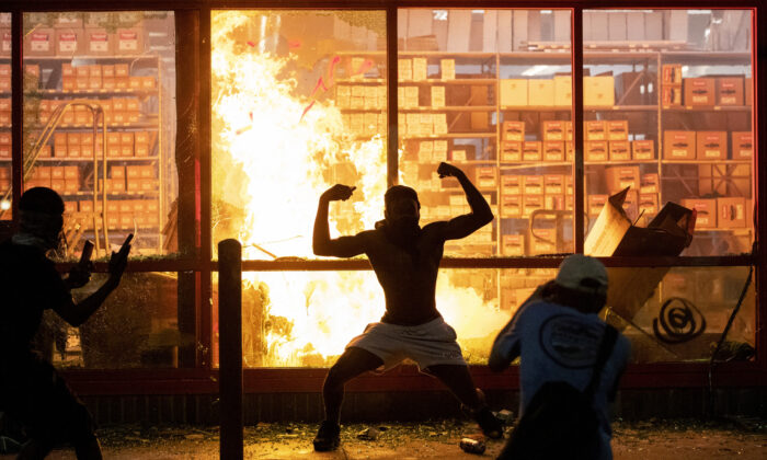 A man poses for photos in front of a fire at an AutoZone store, while protesters hold a rally for George Floyd in Minneapolis on May 27, 2020. (Carlos Gonzalez/Star Tribune via AP)