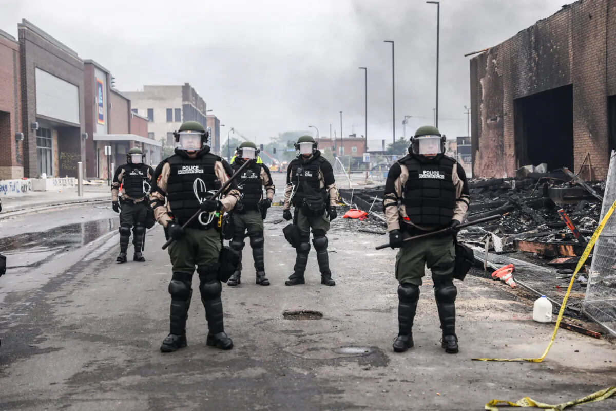 Police officers stand near burned out buildings in the aftermath of a night of protests and violence following the death of George Floyd, in Minneapolis, Minn., on May 29, 2020. (Charlotte Cuthbertson/The Epoch Times)