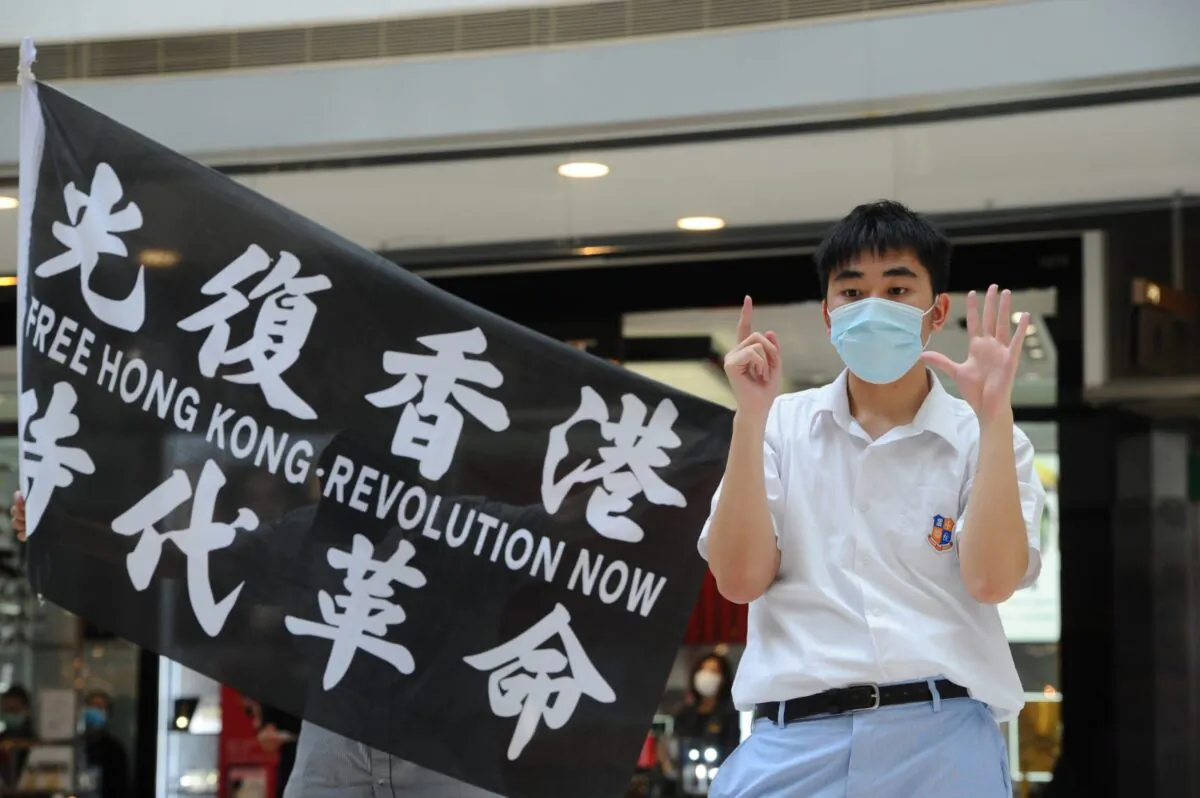A protester stands next to a flag with the words “Free Hong Kong, Revolution Now” at a protest at the IFC shopping mall in Hong Kong on May 29. 2020. (Song Bilung/The Epoch Times)