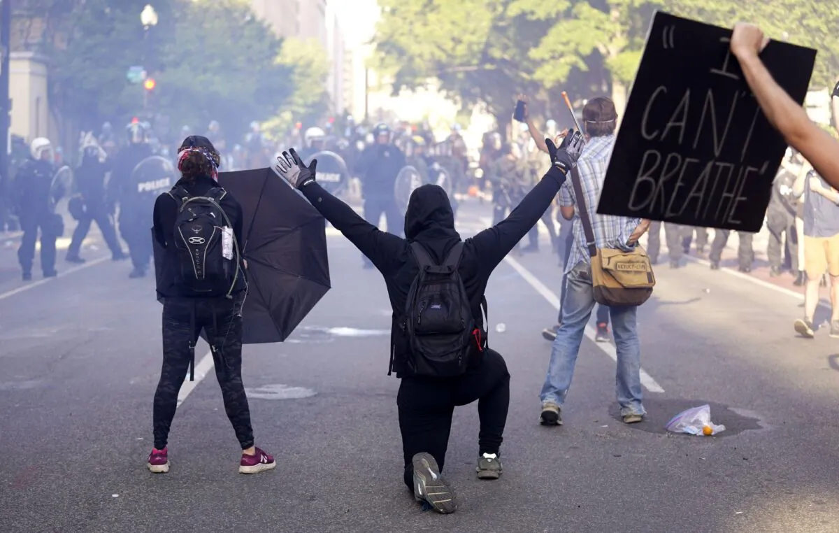 A demonstrator kneels in front of a line of police officers as smoke drifts in the air during a protest over the death of George Floyd, near the White House in Washington on June 1, 2020. (AP Photo/Evan Vucci)