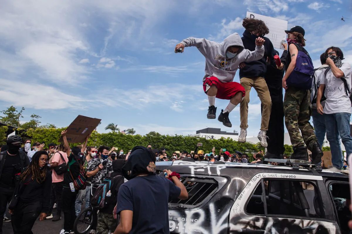 Demonstrators jump on a damaged police vehicle in Los Angeles on May 30, 2020, during a protest following the death of George Floyd. (Ariana Drehsler/AFP via Getty Images)
