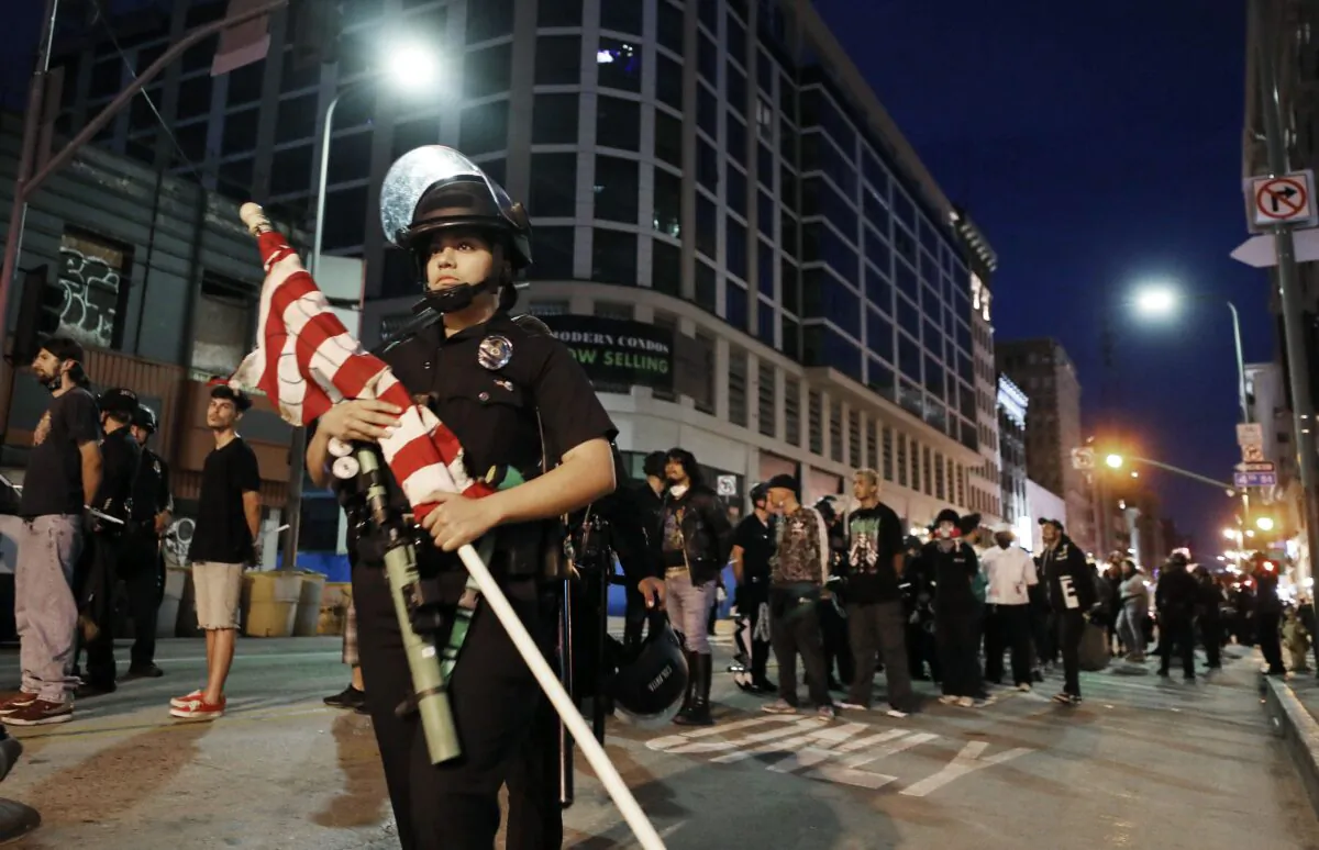 Protesters stand handcuffed under arrest after curfew as a police officer carries away an American flag in Los Angeles, Calif. on June 2, 2020. (Mario Tama/Getty Images)