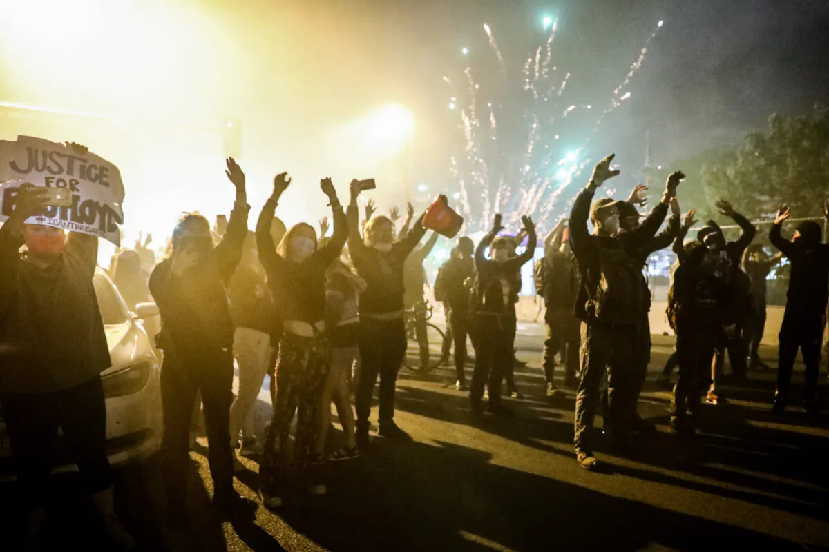 Protesters face police as the latter move in with tear gas to take over the chaotic streets outside the Minneapolis Police 5th Precinct during the fourth night of protests and violence following the death of George Floyd, in Minneapolis, Minn., on May 29, 2020. (Charlotte Cuthbertson/The Epoch Times)