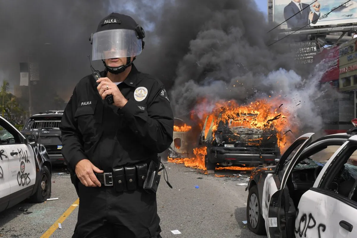 Los Angeles Police Department commander Cory Palka stands among several destroyed police cars as one explodes while on fire during a protest over the death of George Floyd in Los Angeles, Calif. on May 30, 2020. (Mark J. Terrill/AP Photo)