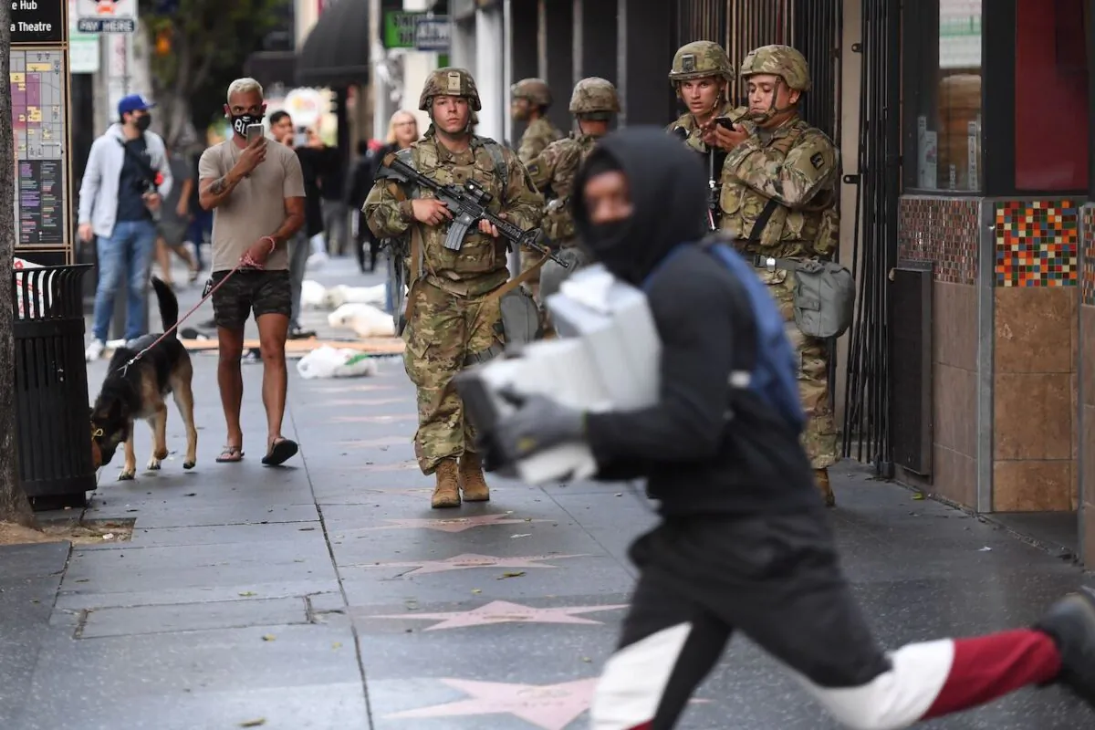 A suspected looter carrying boxes of shoes runs past National Guard soldiers in the Hollywood area of Los Angeles on June 1, 2020. (Robyn Beck/AFP via Getty Images)