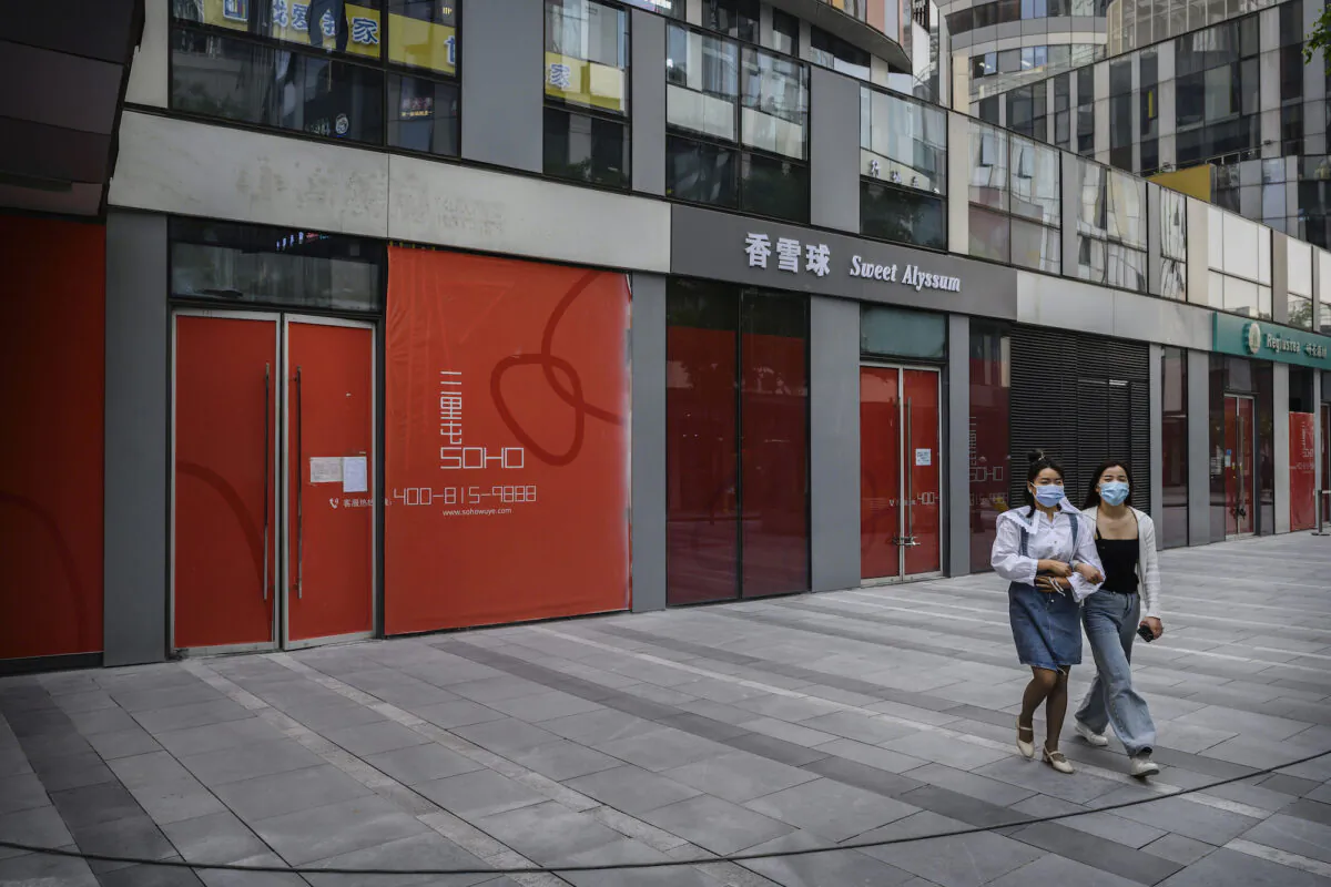 Chinese women wear protective masks as they walk by shops that have gone out of business, in a shopping district in Beijing on April 28, 2020. (Kevin Frayer/Getty Images)