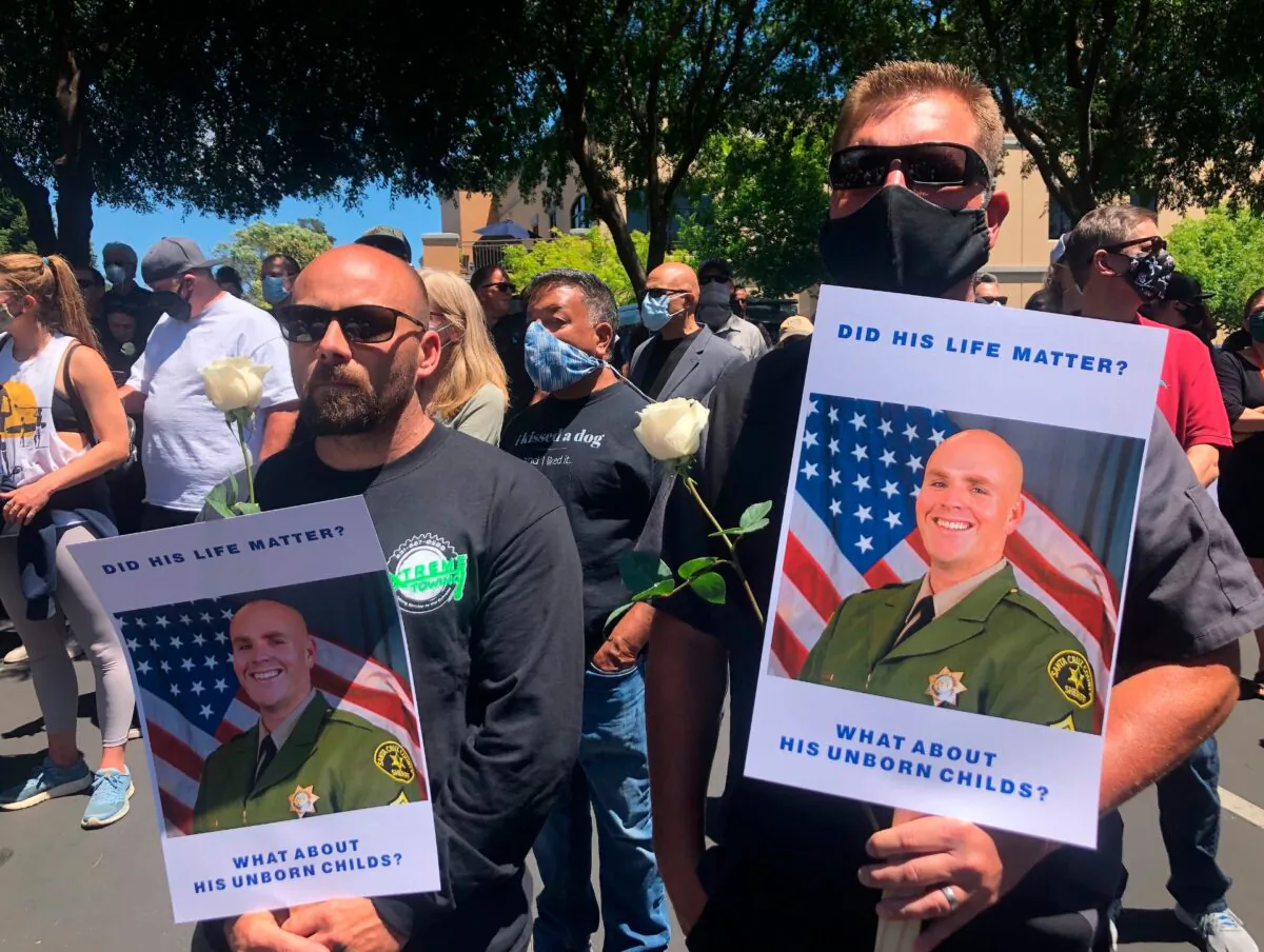 Matthew Rose (L) and Michael Carr, of Santa Cruz County hold posters of slain Sgt. Damon Gutzwiller, as they join others outside the Santa Cruz County Sheriff-Coroner's Office to pay their respects in Santa Cruz, Calif., on June 7, 2020. (Martha Mendoza/AP Photo)