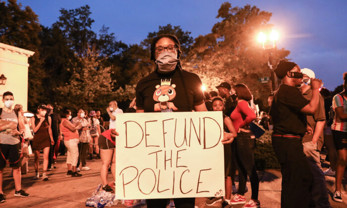 A protester holds a “Defund the Police” sign during a protest near the White House following the May 25 death of George Floyd in police custody, in Washington on June 6, 2020. (Charlotte Cuthbertson/The Epoch Times)