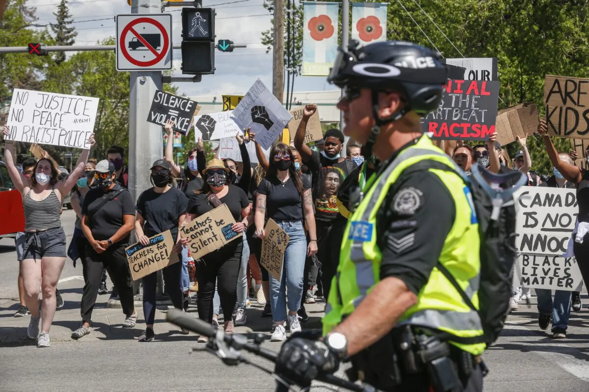 A police officer looks on as protesters march in solidarity with the George Floyd protests across the United States, in Calgary, Alta., on June 3, 2020. (The Canadian Press/Jeff McIntosh)