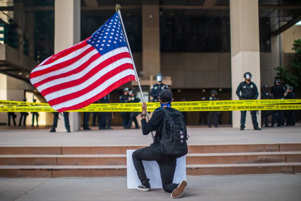 A demonstrator holding a flag kneels in front of the police at the Anaheim City Hall during a peaceful protest over the death of George Floyd in Anaheim, Calif., on June 1, 2020. (Apu Gomes/AFP via Getty Images)