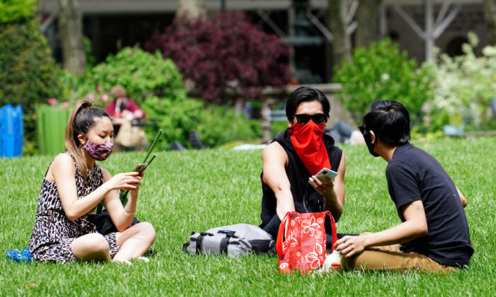 Three people wear protective masks while sitting on the lawn in Bryant Park during the CCP virus pandemic in New York City on May 22, 2020. (Cindy Ord/Getty Images)