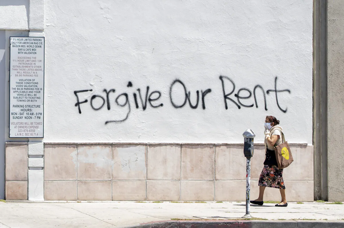 A woman wearing a mask walks past a wall bearing graffiti that asks for rent forgiveness amid the COVID-19 pandemic, in Los Angeles on May 1, 2020. (Valerie Macon/AFP via Getty Images)