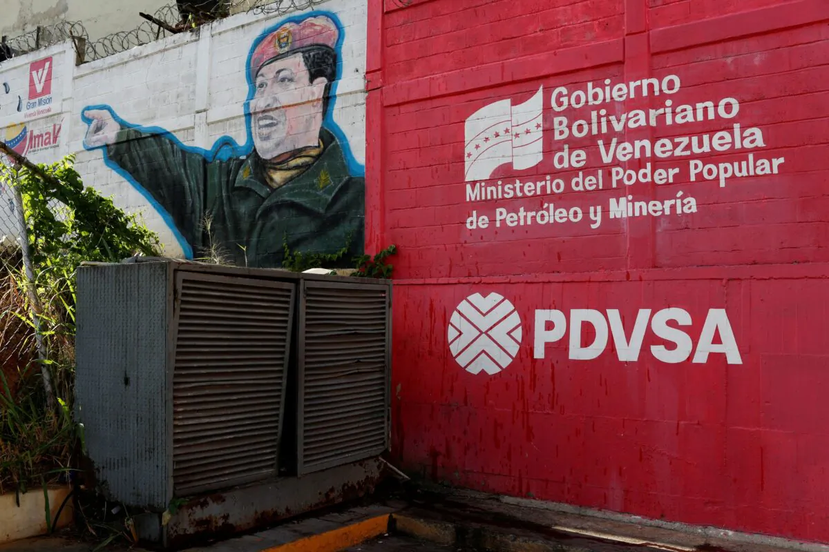 The logo of the Venezuelan state oil company PDVSA is seen next to a mural depicting Venezuela's late President Hugo Chavez at a gas station in Caracas, Venezuela, on March 2, 2017.  (Carlos Garcia Rawlins/Reuters)