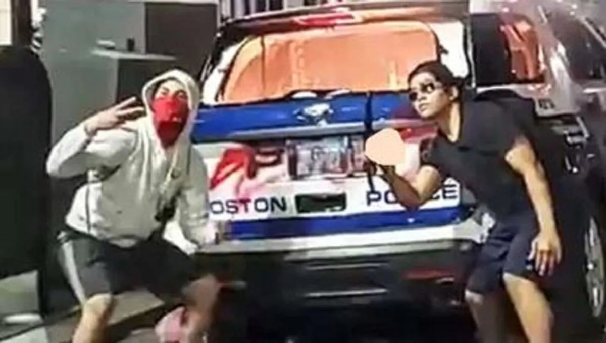 Two males pose in front of a police car that was vandalized and set on fire in Boston, Mass., on May 31, 2020. (FBI)