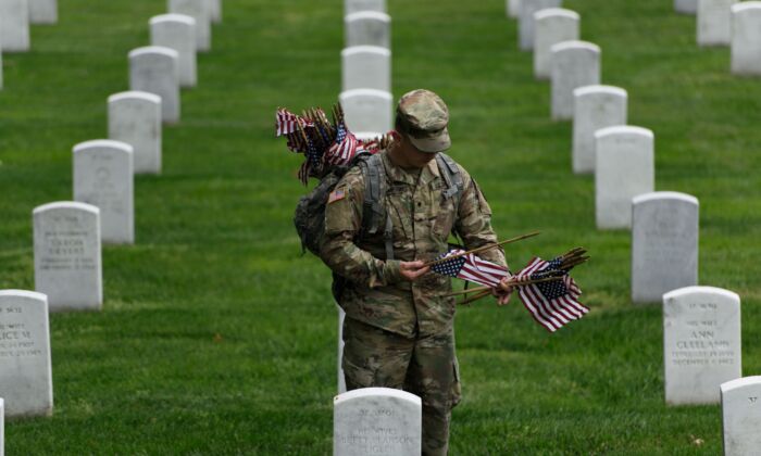 A member of the U.S. Army places American flags on a grave at Arlington National Cemetery on May 25, 2017. (Brendan Smialowski/AFP via Getty Images)