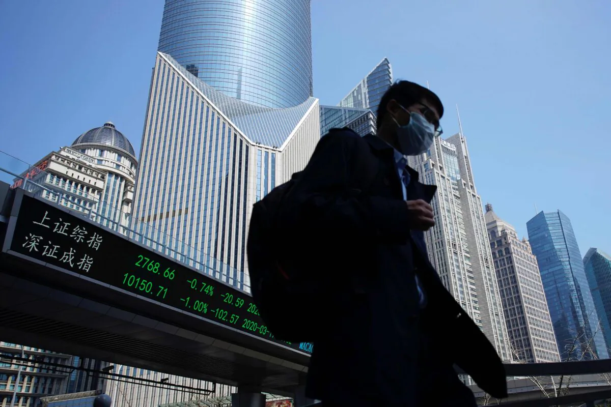 A pedestrian wearing a face mask walks near an overpass with an electronic board showing stock information, following an outbreak of COVID-19 at Lujiazui financial district in Shanghai on March 17, 2020. (Aly Song/Reuters)