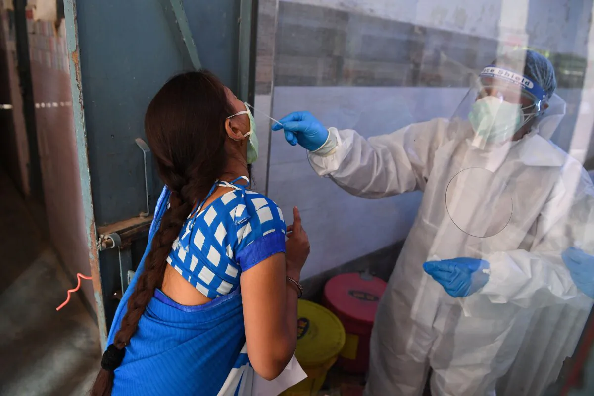 A medical staff (R) wearing personal protective equipment collects a nasal swab with a rapid antigen test for the CCP virus at a testing center after the government eased a nationwide lockdown as a preventive measure against COVID-19, in New Delhi on June 19, 2020. (Prakash Singh/AFP/Getty Images)