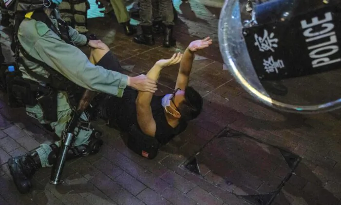 A police officer (L) detains a man (C) as protesters gathered in the Mong Kok district of Hong Kong on June 12, 2020. (Isaac Lawrence/AFP via Getty Images)