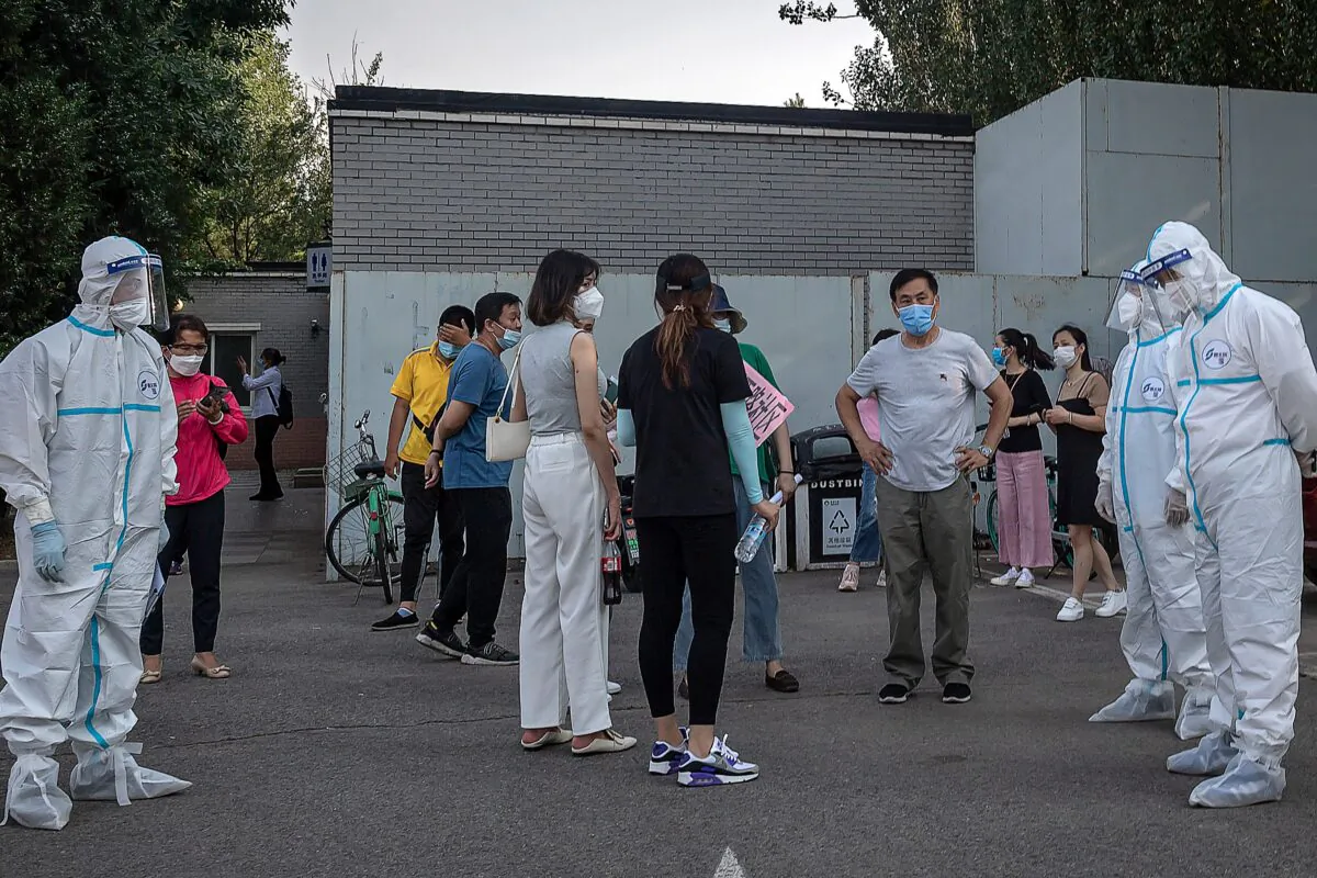 Workers wearing personal protective equipment take care of a group of people wearing face masks as they wait to undergo COVID-19 tests in Beijing on June 19, 2020. (NICOLAS ASFOURI/AFP via Getty Images)