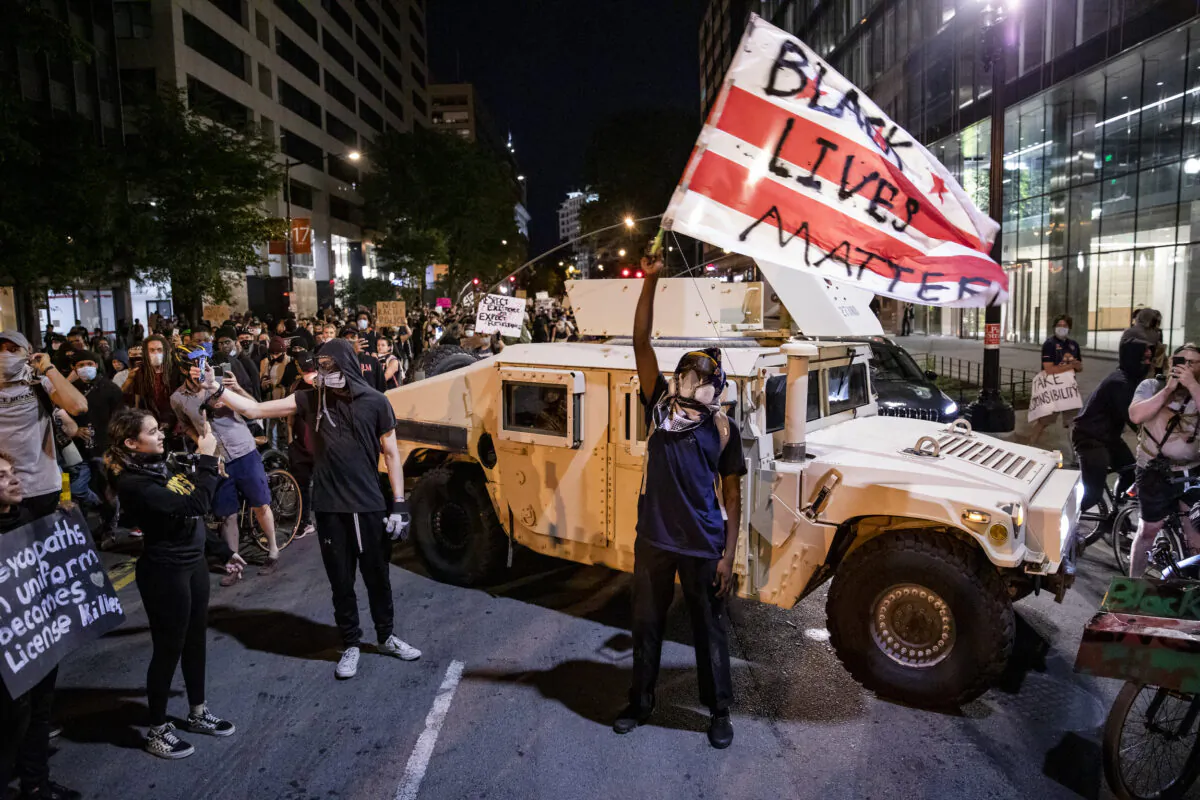 A protester waves a DC flag with “Black Lives Matter” spray painted on it next to a DC National Guard Humvee during a demonstration over the death of George Floyd, who died in police custody, in Washington on June 2, 2020. (Samuel Corum/Getty Images)