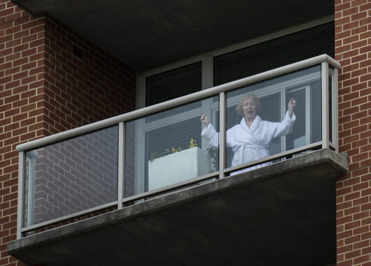 A resident of a senior living community dances on her balcony as she listens to a DC area motown band play a social distance concert in the community’s parking lot in Arlington, Va., on April 14, 2020. (Andrew Caballero-Reynolds/AFP via Getty Images)