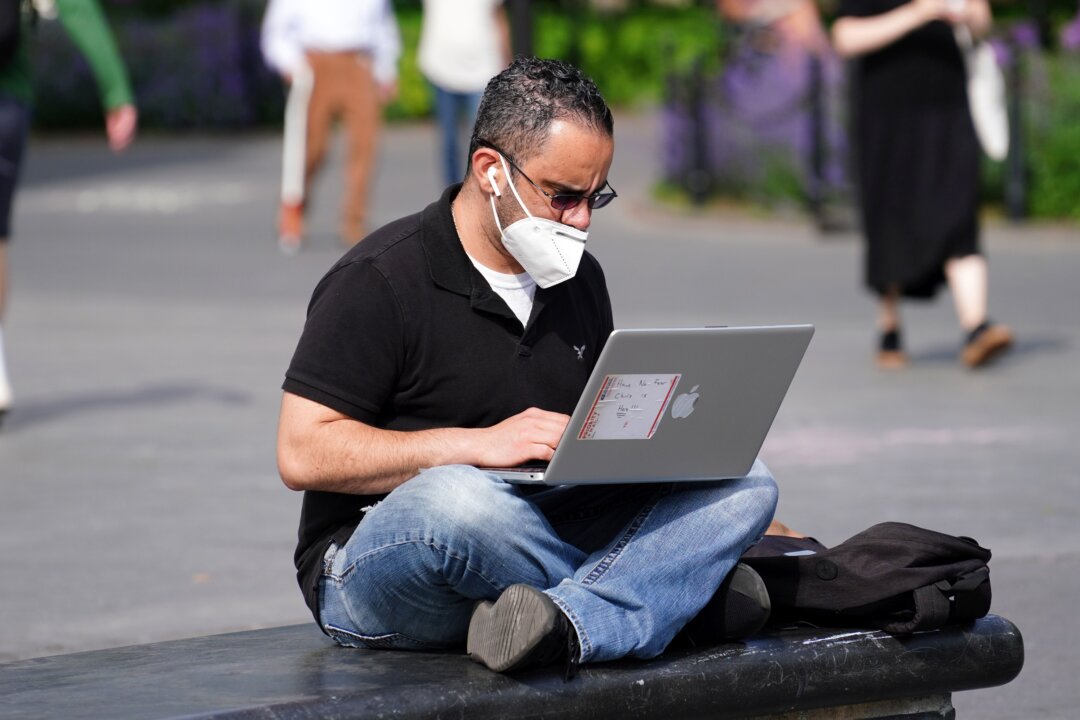 A man wearing a mask uses a laptop, in this file photo. (Cindy Ord/Getty Images)