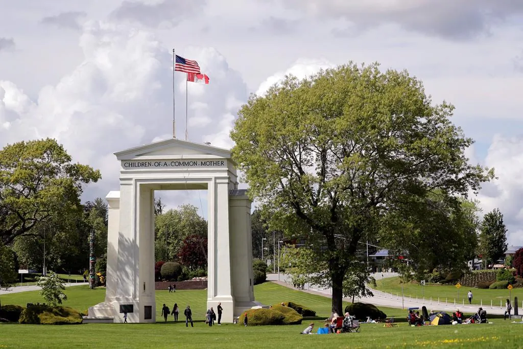 In this photo taken May 17, 2020, people walk back and forth across the border between the United States and Canada in Peace Arch Park in Blaine, Washington. (The Canadian Press/AP-Elaine Thompson)