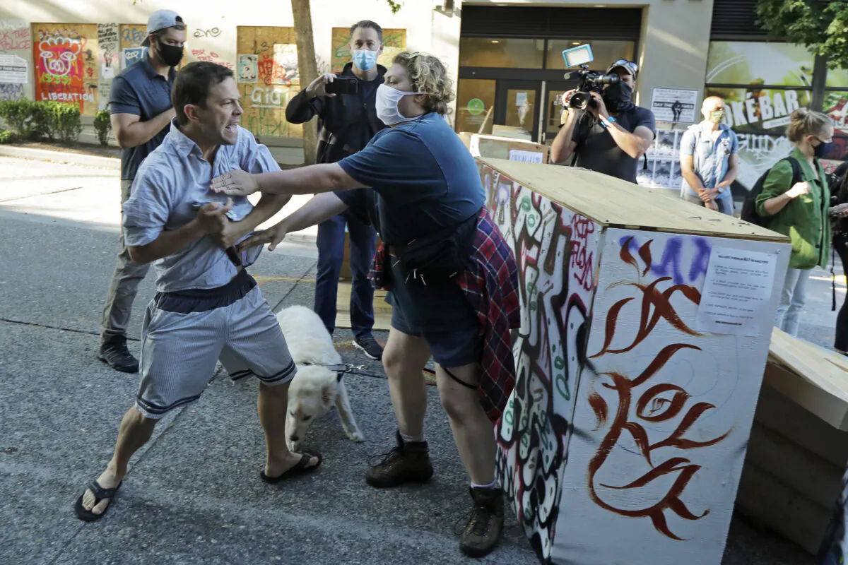A person tries to take away a hammer from a man at left who was using it to remove artwork on barricades at the CHOP (Capitol Hill Occupied Protest) zone in Seattle, Wash., on June 26, 2020. (Ted S. Warren/AP Photo)