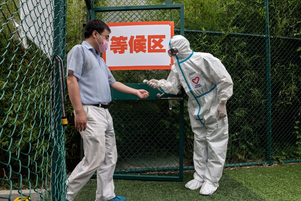 A man wearing a face mask gets his body temperature checked by a health worker wearing personal protective equipment as he walks into an outdoor area during a mass testing for the COVID-19 coronavirus at the Xinjiekou urban forest park testing site in Beijing on June 24, 2020. (Nicolas Asfouri/AFP via Getty Images)