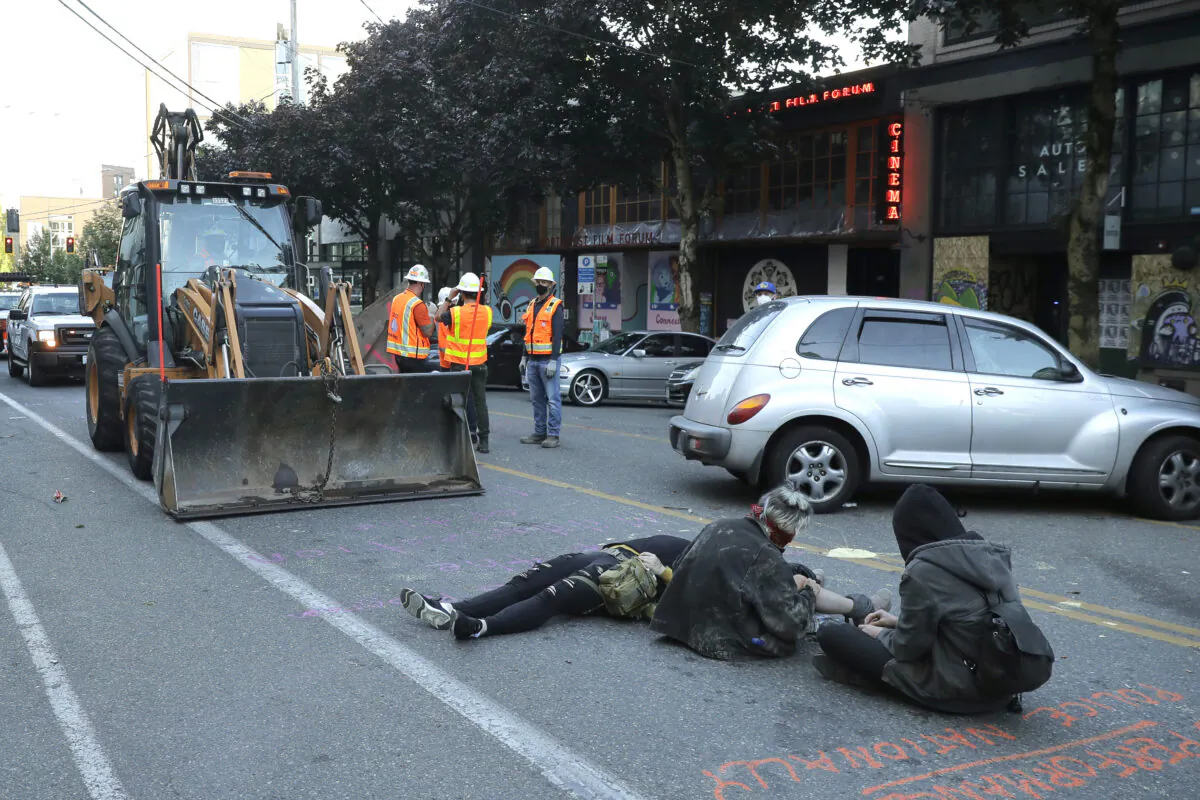 Protesters lie down and sit in the street after workers and heavy equipment from the Seattle Department of Transportation arrived at the the CHOP (Capitol Hill Occupied Protest) zone in Seattle, Wash., on June 26, 2020. (Ted S. Warren/AP Photo)