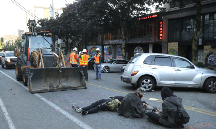 Protesters lie down and sit in the street after workers and heavy equipment from the Seattle Department of Transportation arrived at the the CHOP (Capitol Hill Occupied Protest) zone in Seattle, Wash., on June 26, 2020. (Ted S. Warren/AP Photo)