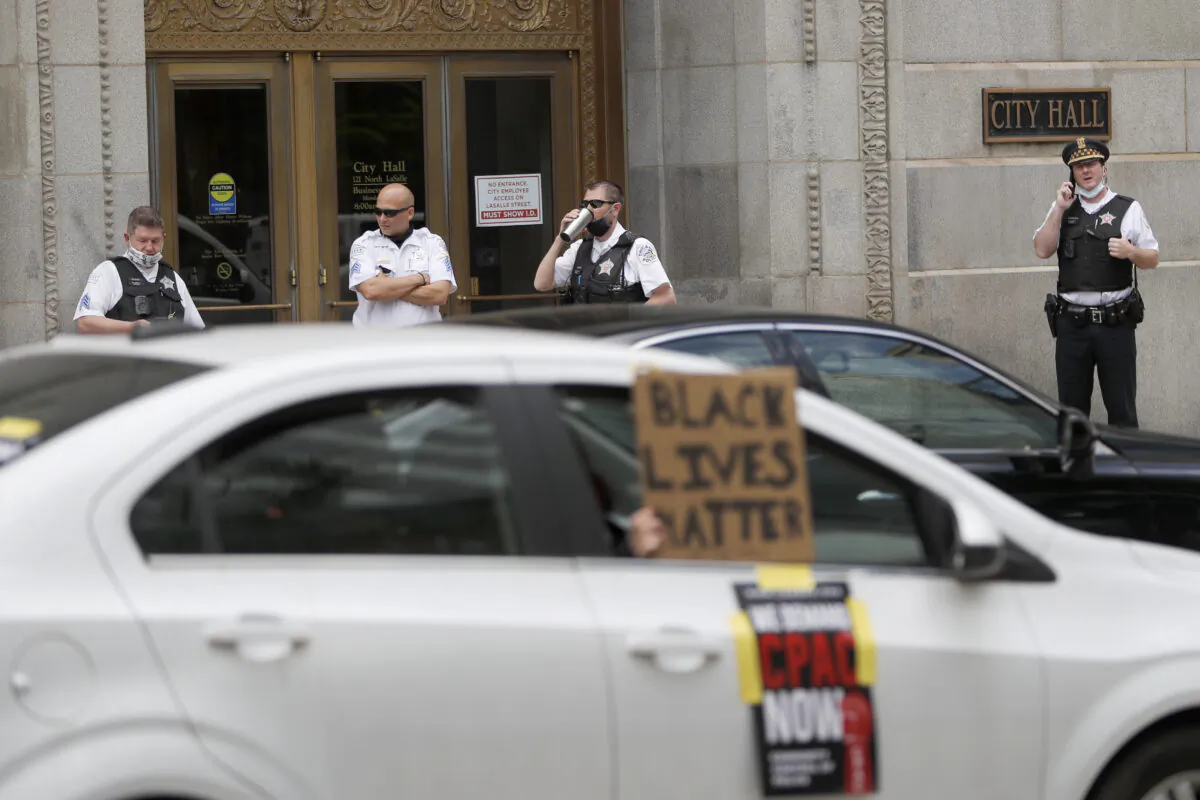 Chicago police officers stand outside City Hall, watching as a caravan of protesters demand that Mayor Lori Lightfoot enact the ordinance for an all-elected Civilian Police Accountability Council, CPAC, on June 17, 2020. (Charles Rex Arbogast/AP Photo)