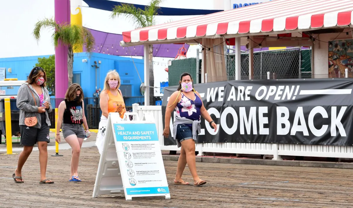 People wearing facemasks walk past a health and safety guideline board and an open restaurant on Santa Monica Pier which re-opened on June 25 after closure for over three months due to the pandemic in Santa Monica, Calif., on June 26, 2020. (FREDERIC J. BROWN/AFP via Getty Images)