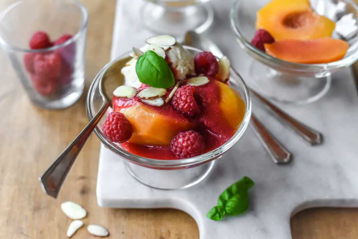 Easy summer elegance: syrup-poached peaches, vanilla ice cream, and raspberry coulis, garnished with slivered almonds and basil. (Photo by Audrey Le Goff)