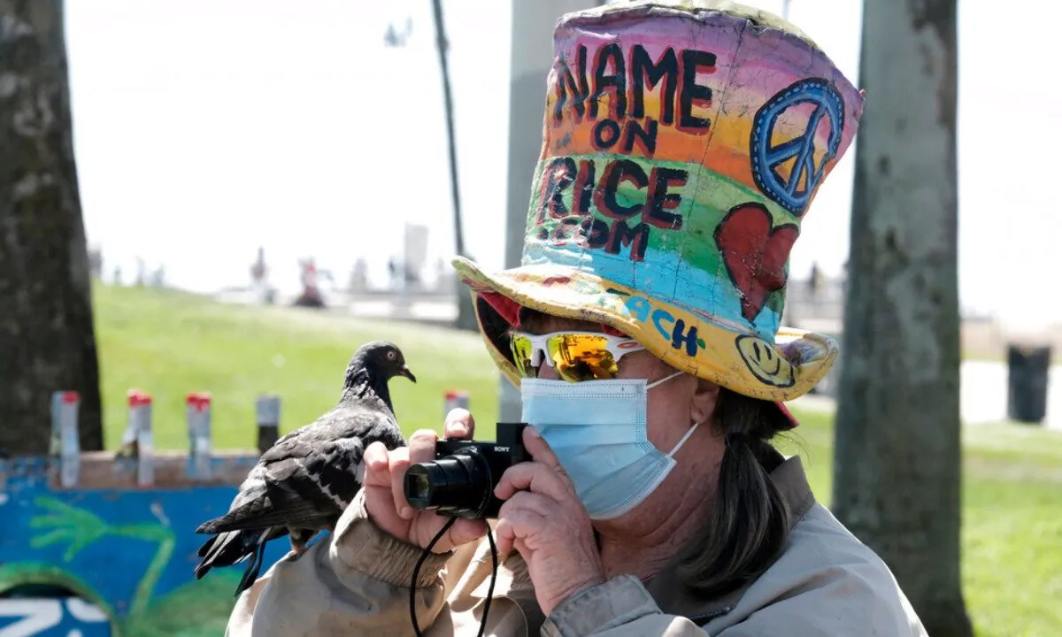 Vendor Vivianne Robinson, wearing a mask to protect from the coronavirus, takes a photo with a pigeon perched on her hand along the Venice Beach strand, on July 3, 2020, in Los Angeles. (Richard Vogel/AP Photo) 
