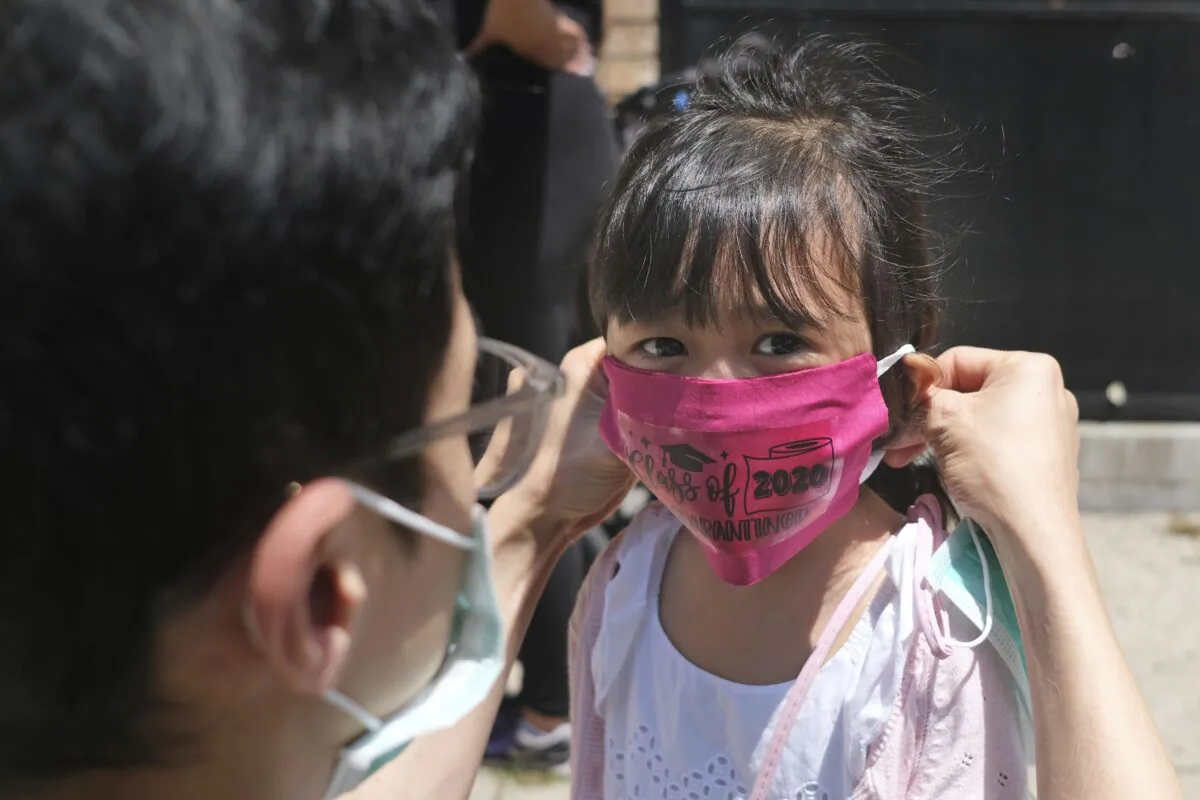 Olivia Chan's father helps her with a new mask she received during a graduation ceremony for her Pre-K class in front of Bradford School in Jersey City, N.J. on June 10, 2020. (Seth Wenig/AP)