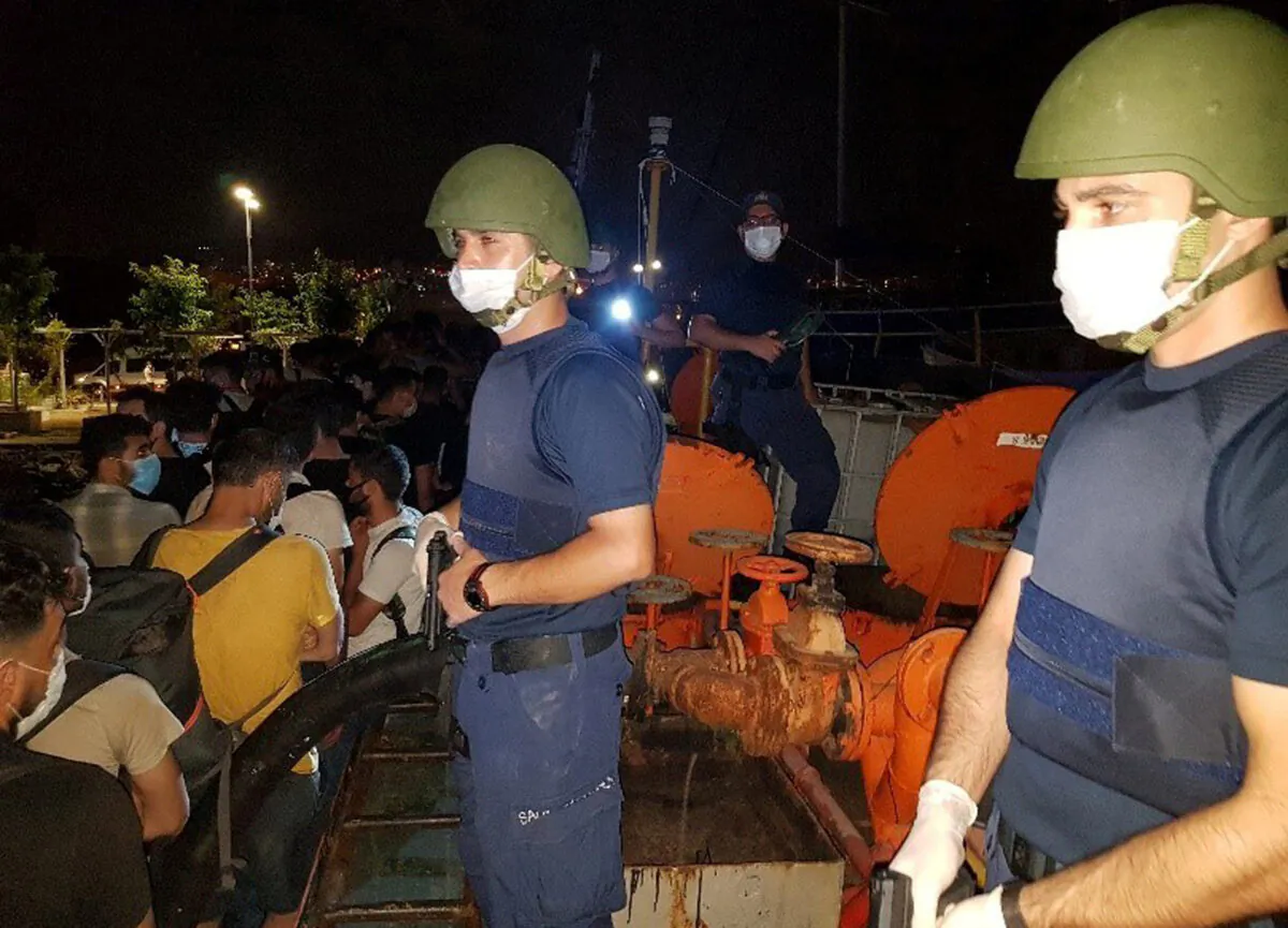 Members of Turkish Coast Guard Command stand guard next to migrants on the deck of a cargo ship during a raid in the Aegean port city of Izmir, Turkey, July 7, 2020. (Turkish Coast Guard Command/Handout via Reuters)