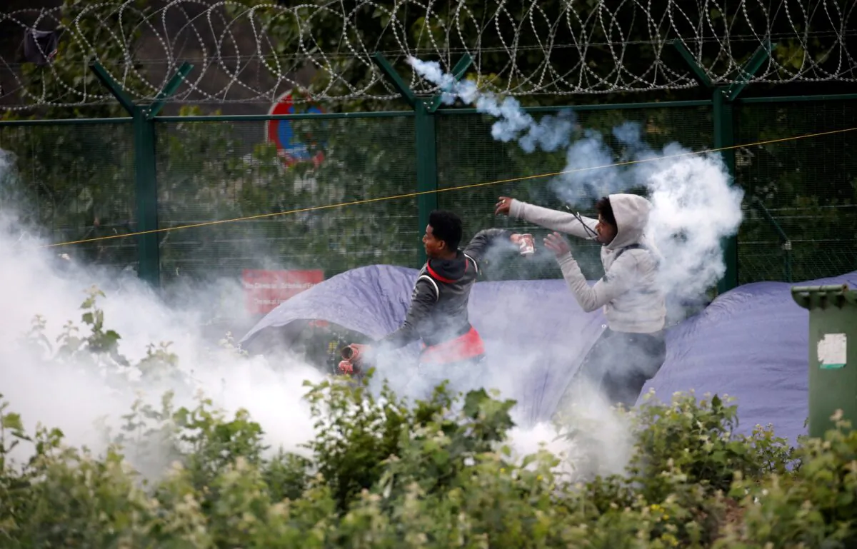 Migrants throw objects at French police officers in a cloud of tear gas as police dismantle a makeshift shelter camp in Calais, France, on July 10, 2020. (Pascal Rossignol/Reuters)