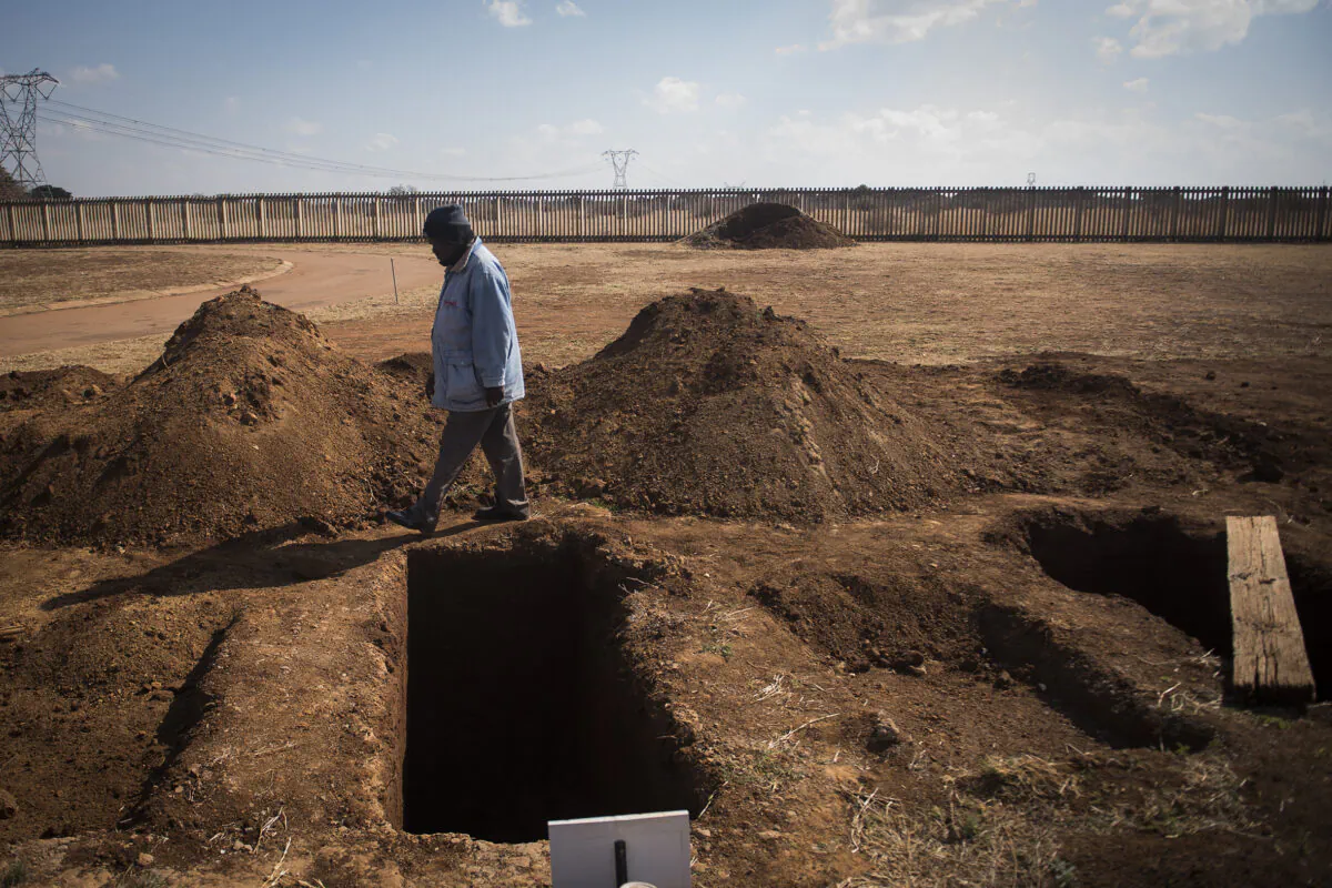 A worker walks past a freshly dug grave at the Honingnestkrans cemetery, near Pretoria, South Africa, on July 9, 2020. (Shiraaz Mohamed/AP)