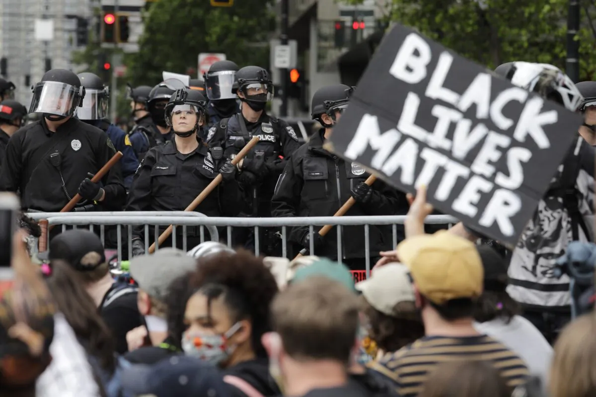 In this June 3, 2020, file photo, police officers behind a barricade look on as protesters fill the street in front of Seattle City Hall, in Seattle. (Elaine Thompson/AP Photo)