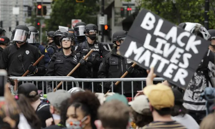 In this June 3, 2020, file photo, police officers behind a barricade look on as protesters fill the street in front of Seattle City Hall, in Seattle. (Elaine Thompson/AP Photo)