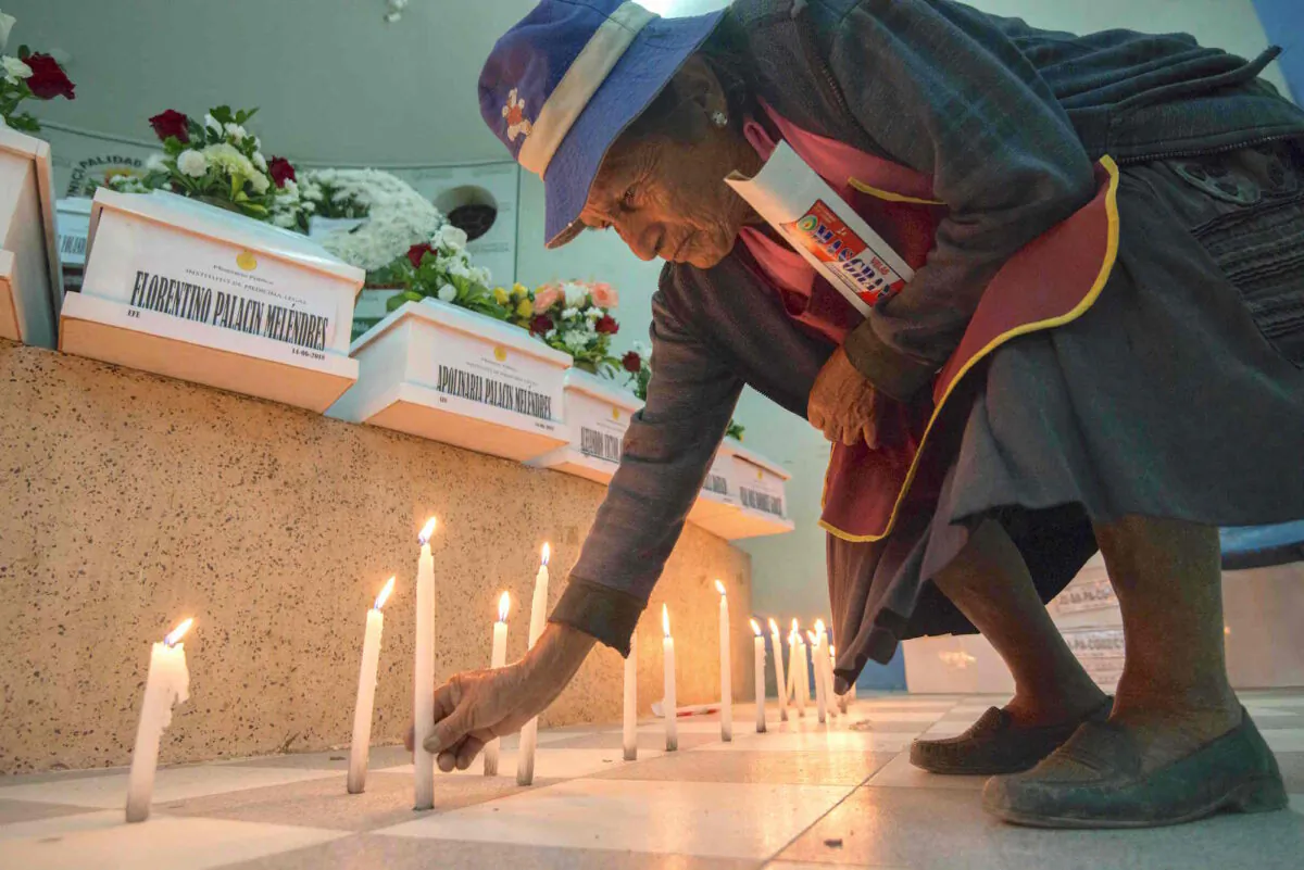 A relative lights a candle in the town of San Martin de Pangoa, Junin Department, Peru, on June 14, 2018 next to coffins containing the remains of 23 identified victims of a massacre by the Shining Path guerrillas in 1990. (CRIS BOURONCLE/AFP via Getty Images)