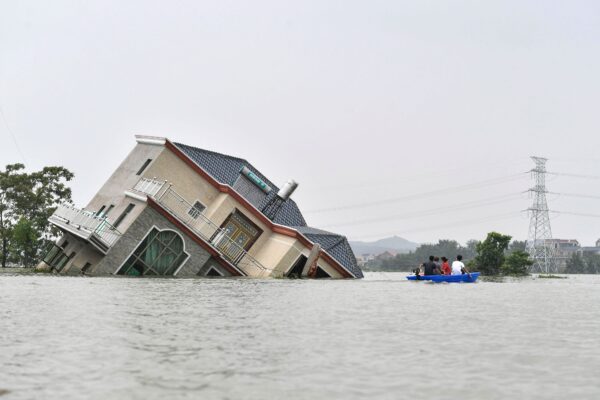 Residents ride a boat past a damaged and flood-affected house