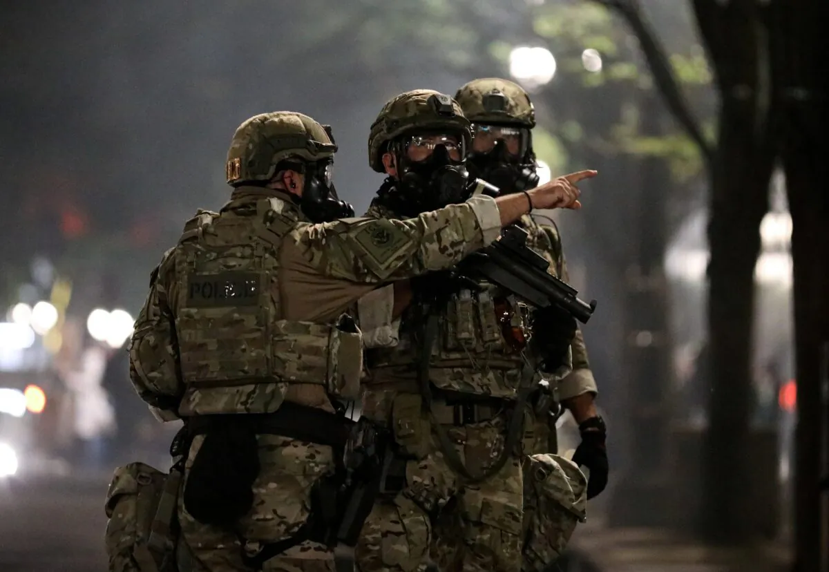 A federal law enforcement official points to demonstrators before firing tear gas during a riot in Portland, Ore., on July 19, 2020. (Caitlin Ochs/Reuters)